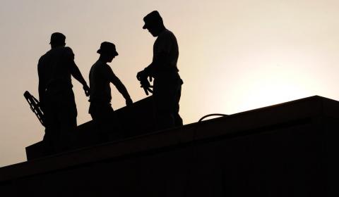 Vue en contre-jour d'ouvriers travaillant sur un toit.