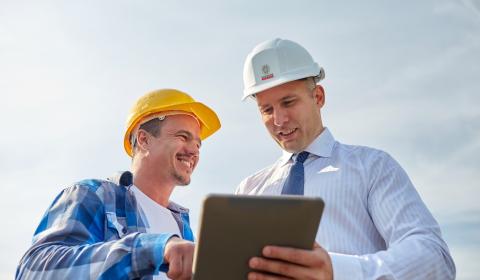 Un chef de chantier et un architecte discutant sur le terrain à l'aide d'une tablette