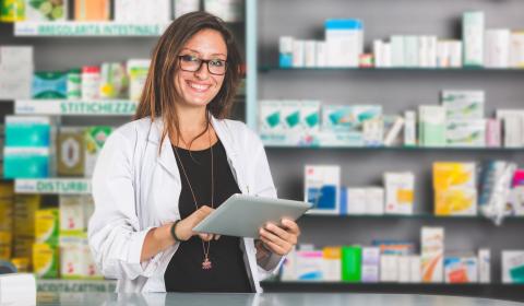 Une pharmacienne souriante à son poste tenant une tablette numérique entre les mains